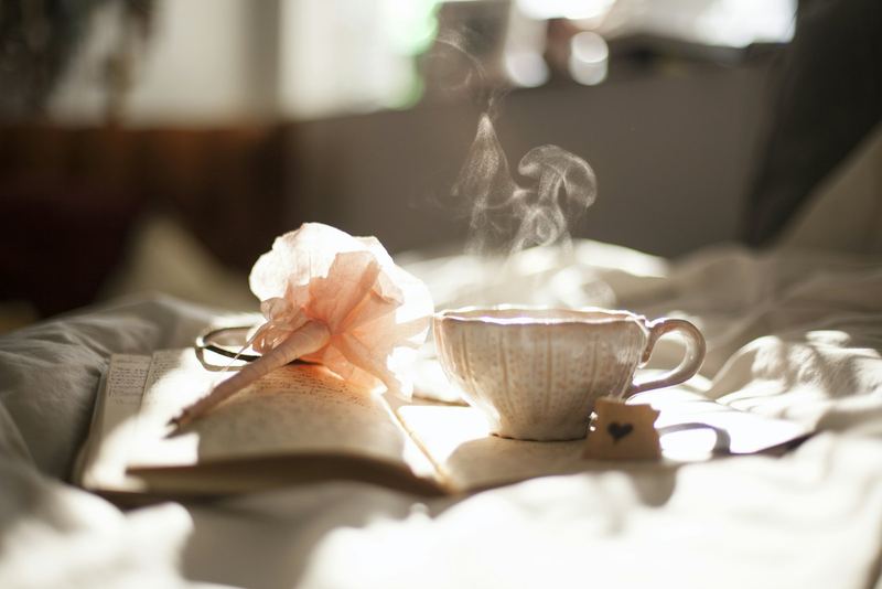 Dampfende Teetasse neben Rosen und Buch